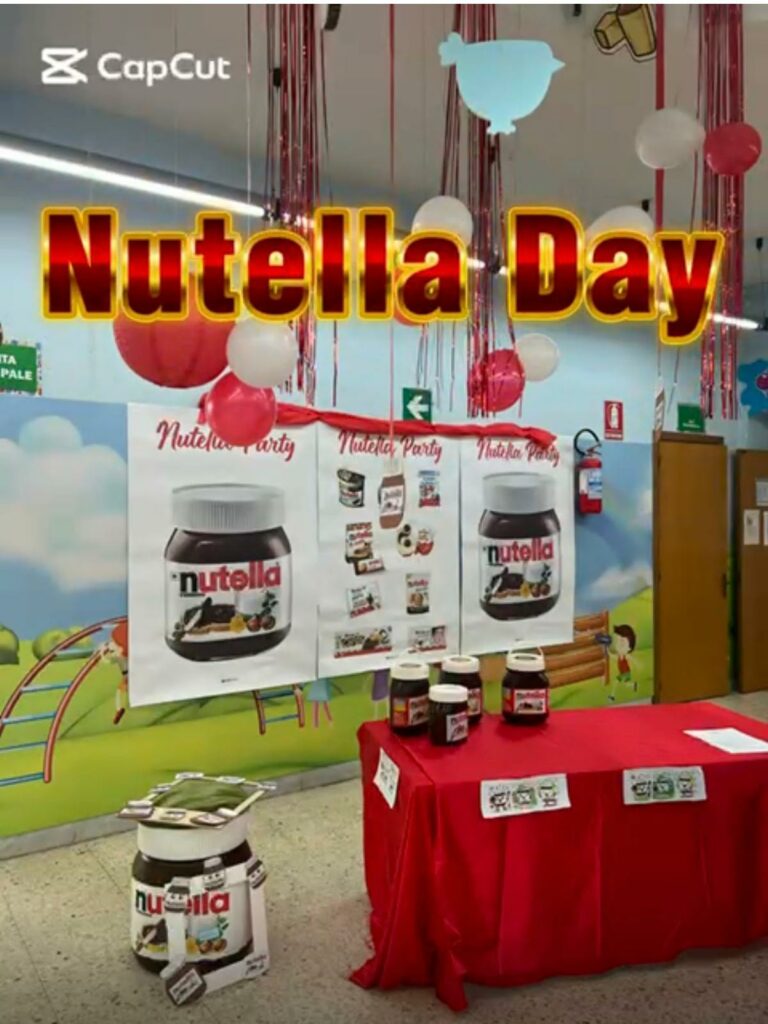 Allestimento per l'evento scolastico 'Nutella Day' con un tavolo coperto da una tovaglia rossa, barattoli di Nutella e cartelloni a tema appesi alla parete decorata con palloncini.
