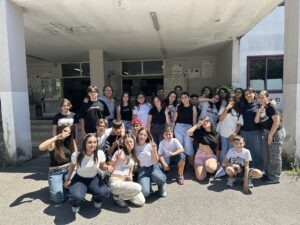 Un gruppo numeroso di studenti, studentesse e due docenti sorridenti che posano insieme all'esterno dell'edificio scolastico subito dopo la conclusione del webinar internazionale.