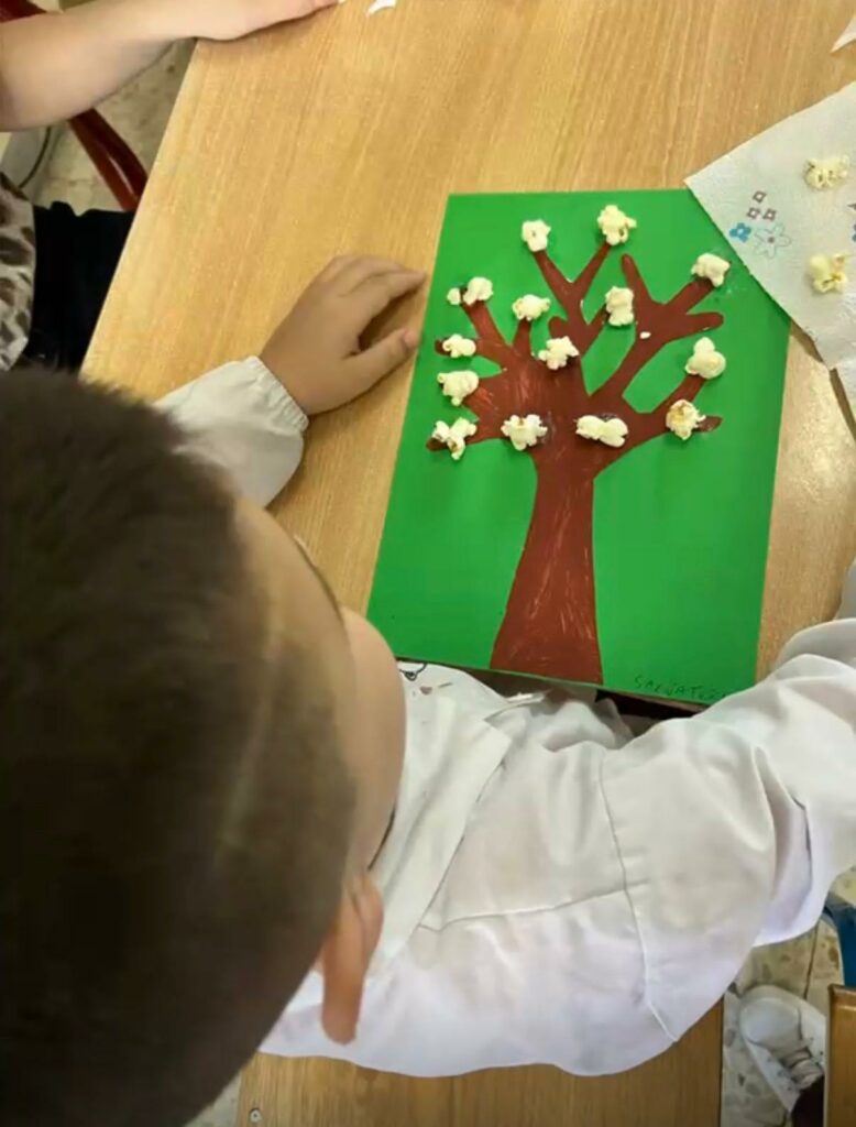 Bambino impegnato in un laboratorio creativo durante la Giornata della Creatività, mentre incolla dei popcorn su un disegno di un albero realizzato su cartoncino verde
