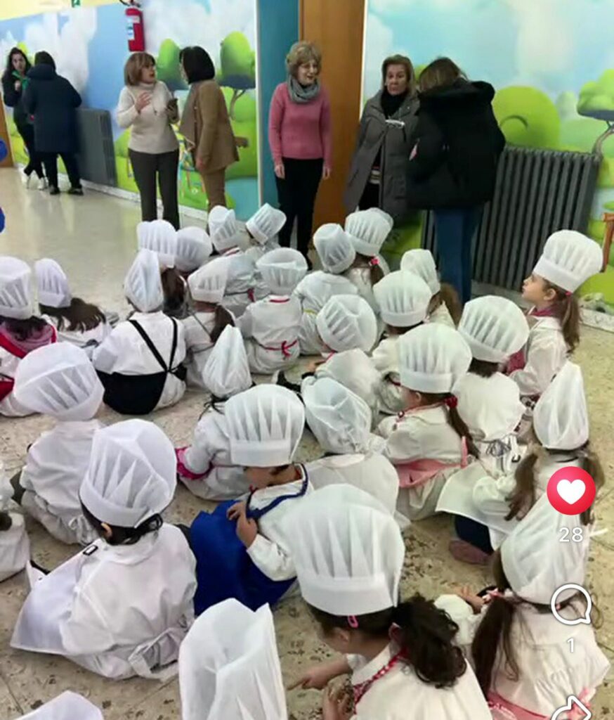 alunni dell'infanzia con cappello e grembiule da cuoco seduti per terra 