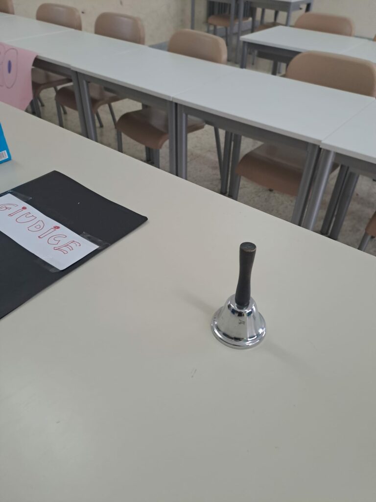 Setting del Debate: Il tavolo del giudice con quaderno e campanello"